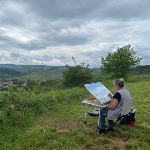 Landschaftsmalerin Heike Negenborn sitzt im Freien an ihrer Staffelei und malt 
