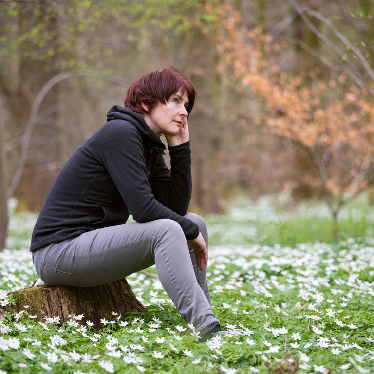 Frau sitzt auf einem Baumstumpf im Frühlingswald (Foto: IMAGO, Dieter Mendzigall)
