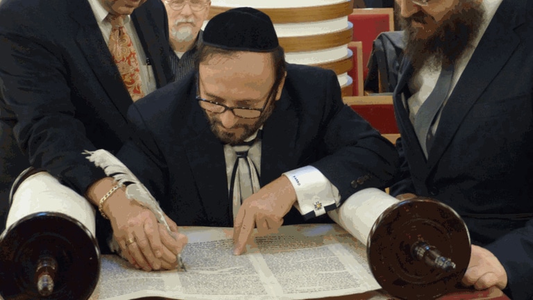 „Signing the Thora 11272013 in Berlin“, notiert Leonard Wien (links). Er führt die Hand des Thoraschreibers Steve Karro bei dieser Rolle, während er die letzten Buchstaben mit der Gänsefeder setzt. Rechts Rabbiner Yehuda Teichtal.