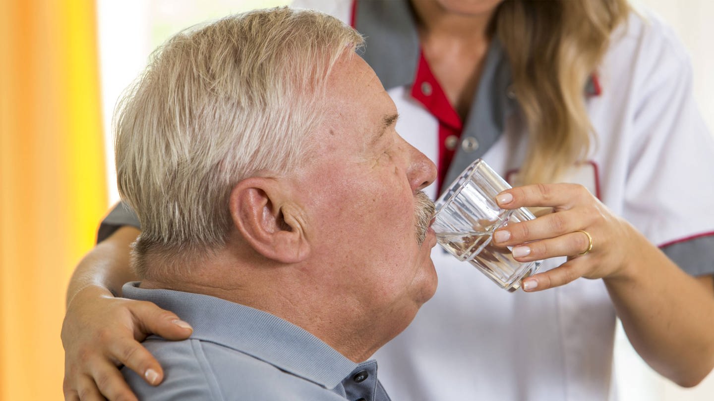 Eine Altenpflegerin hilft einem älteren Mann beim Trinken (Foto: IMAGO, imago/Jochen Tack)