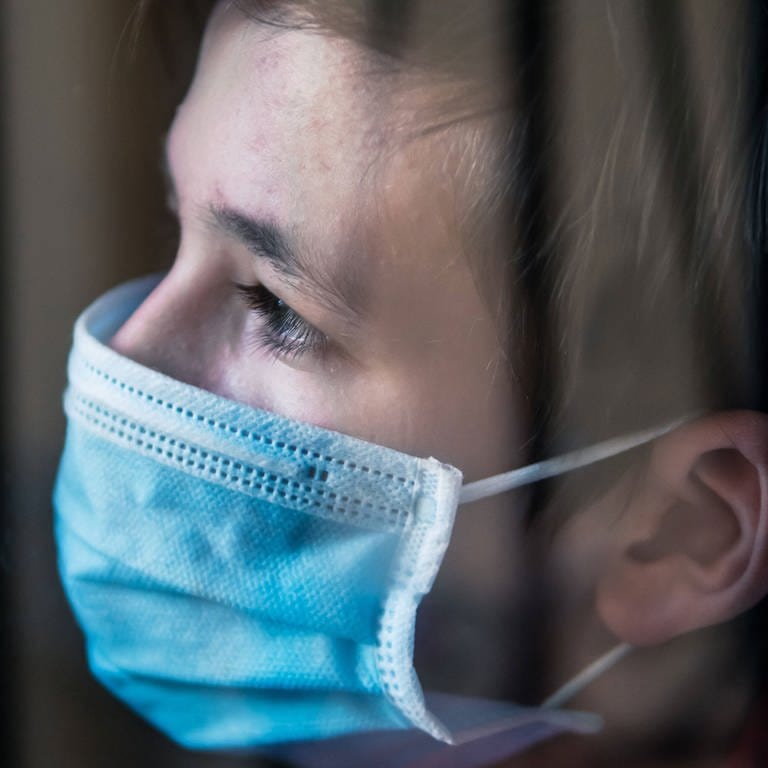 Trauriger Junge mit medizinischer Gesichtsmaske hinter einem Fenster  (Foto: IMAGO, imago images/CHROMORANGE/)