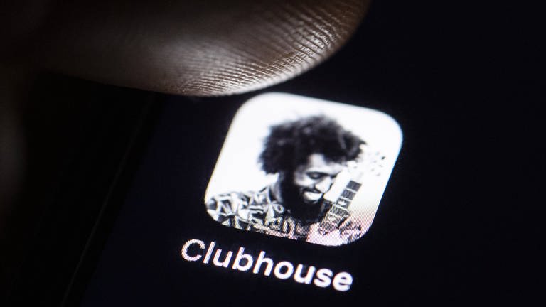Ein Finger steht kurz davor auf das Icon der Social-Media-App "Clubhouse" zu tippen. Der Hintergrund ist schwarz.