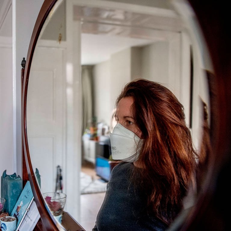 Eine junge Frau mit einer Atemschutzmaske betrachtet sich im Spiegel (Foto: IMAGO, imago images/ZUMA Wire/Robin Utrecht )