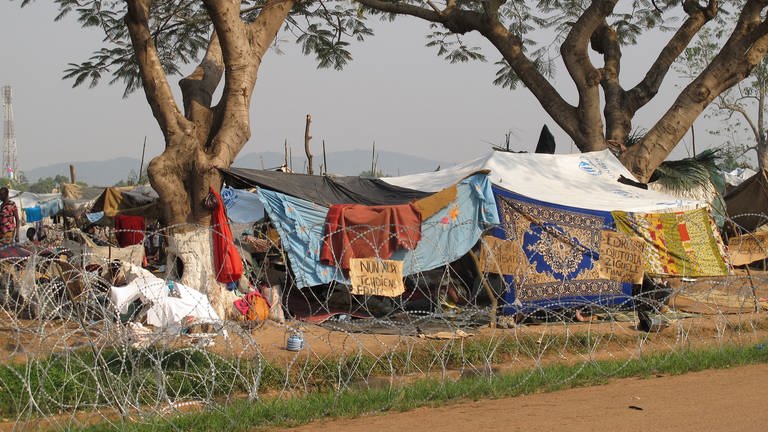 Ein mit Stacheldraht umzäuntes Flüchtlingslager am Rand einer Straße. Als Wände und Dächer dienen Tücher und Planen vom UNHCR (Foto: Antje Diekhans)