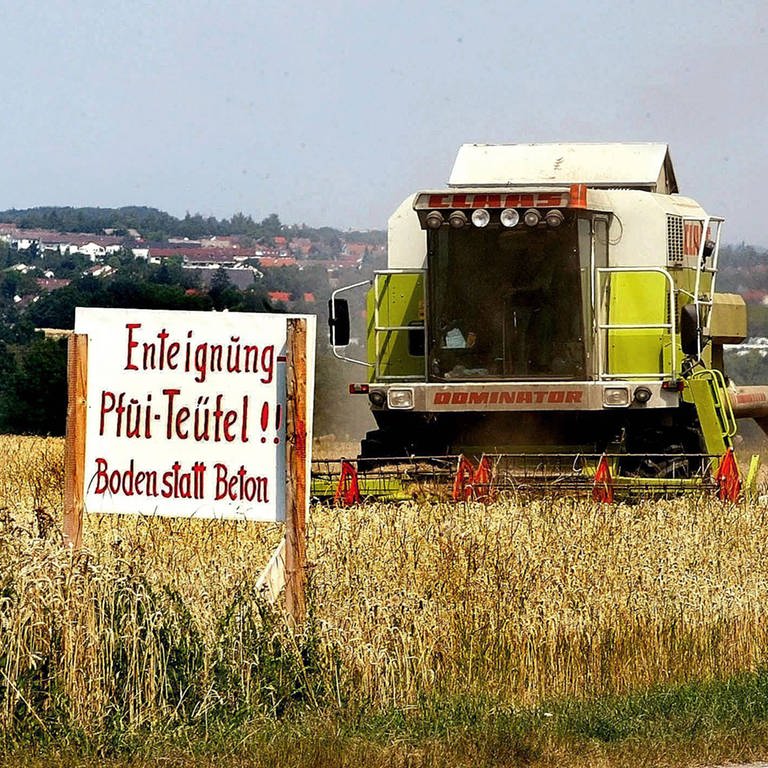 Mähdrescher bei der Ernte hinter einem Schild mit dem Schriftzug - Enteignung - Pfui Teufel! Boden statt Beton -  in Leinfelden-Echterdingen (Foto: IMAGO, Horst Rudel)