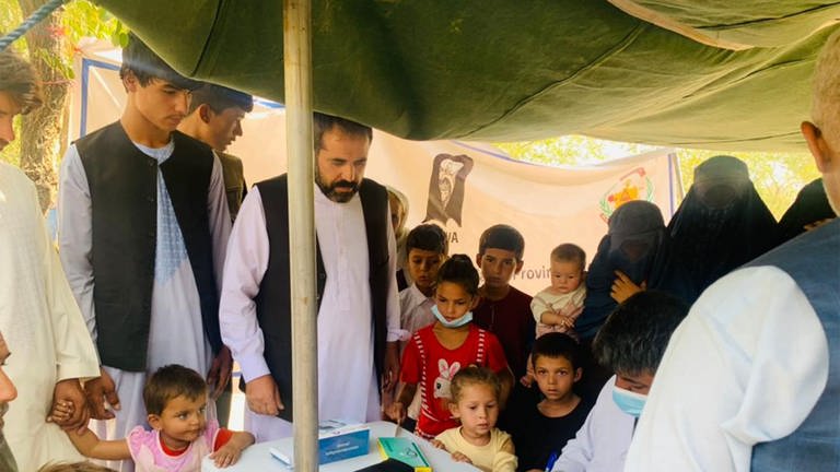 Das Bild zeigt eine mobile Klinik zur medizinischen Versorgung von Binnenvertriebenen in Kabul. Viele Mneschen stehen um einen Tisch herum und möchten die Medizinische Versorgung in Anspruch nehmen.