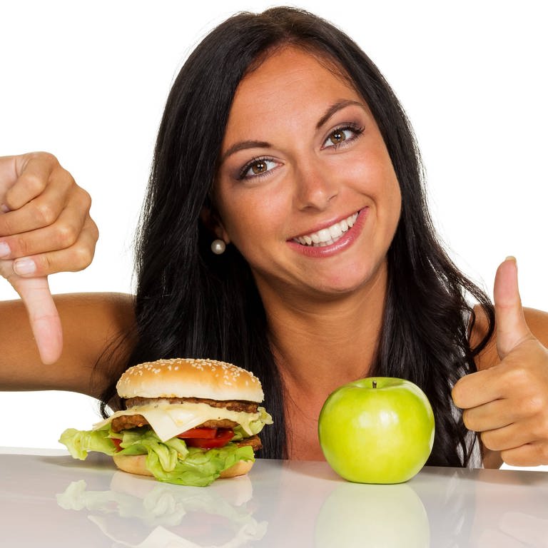 Eine junge Frau kann sich nicht zwischen einem Hamburger und einen Apfel entscheiden. (Foto: IMAGO, IMAGO / McPHOTO)