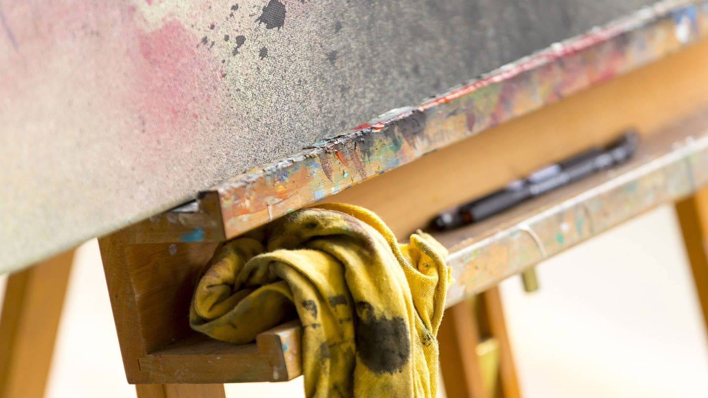 Auf einer Staffelei liegt ein mit Farbe beschmiertes Tuch und Pinsel (Foto: IMAGO, Agentur 54 Grad Felix König)