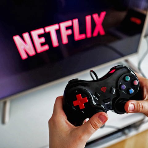 Netflix will sich in Zukunft verstärkt um den Ausbau seiner Gaming-Abteilung kümmern - Hände halten den Controller einer Spielekonsole vor einem TV-Bildschirm auf dem das Netflix-Logo angezeigt wird. (Foto: IMAGO, IMAGO / NurPhoto)