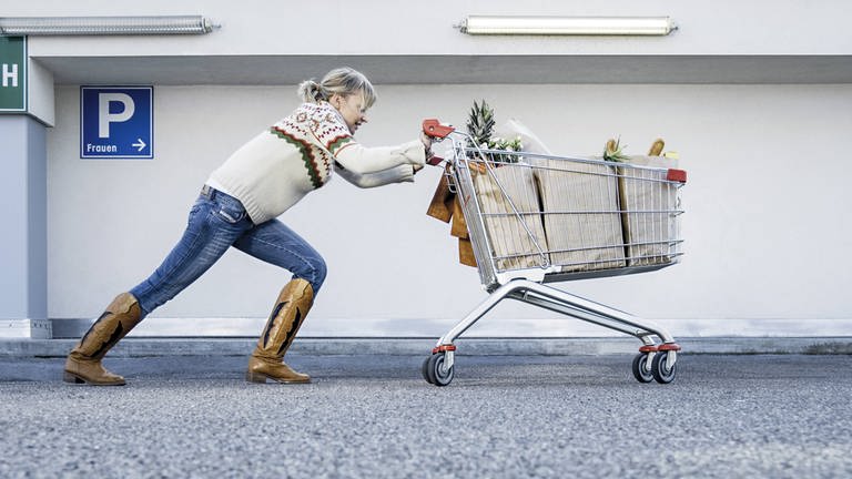 Eine Frau schiebt einen Einkaufswagen mit Weihnachtseinkäufen (Foto: IMAGO, imago images/allOver-MEV)