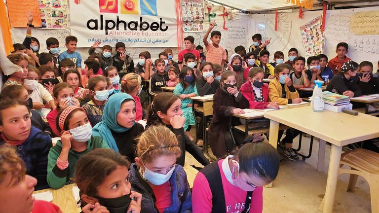 Viele Kinder sitzen dicht gedrängt mit Corona-Masken in der Zeltschule und schauen gespannt nach vorne
