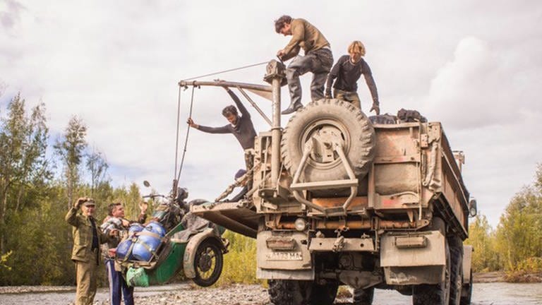 Ein Riesen-Lastwagen hebt mit einem Kran ein Motorradgespann hoch. 6 Männer sind dafür nötig