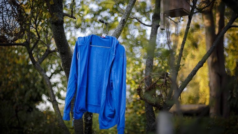 Eine blaue Jacke hängt auf einem Bügel an einem Ast (Foto: IMAGO, Thomas Trutschel/photothek.net)