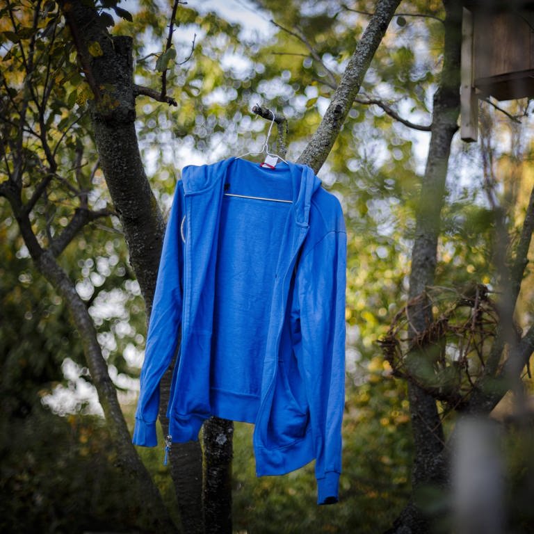 Eine blaue Jacke hängt auf einem Bügel an einem Ast (Foto: IMAGO, Thomas Trutschel/photothek.net)