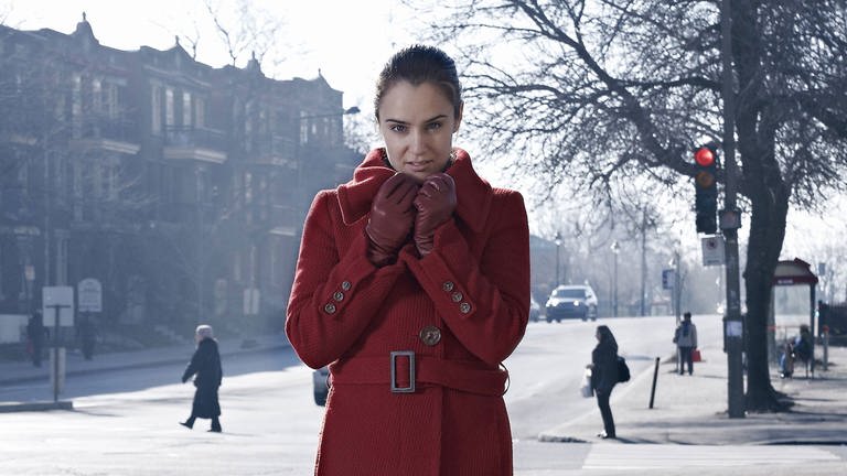 Woman wearing red coat standing at crossroad in gray city model released Symbolfoto