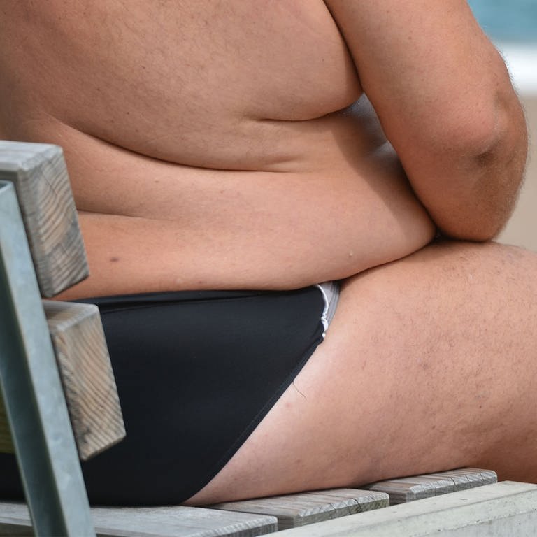 Ein übergewichtiger Mensch sitzt in einem Freibad auf einer Bank (Foto: dpa Bildfunk, picture alliance / Franziska Kraufmann / dpa)
