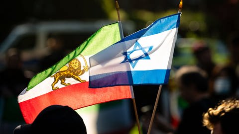 Ein Mann hält eine israelische (r) und eine iranische Fahne