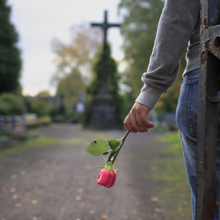 Junge Frau mit einer Rose auf dem Friedhof (Foto: IMAGO, photothek)