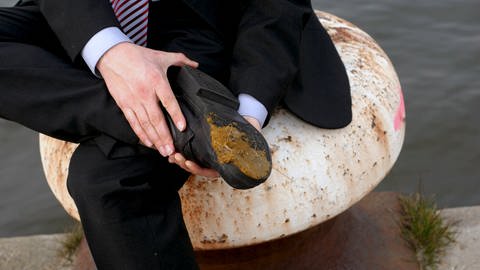 Ein Mann ist in einen Hundehaufen getreten und betrachtet seinen Schuh (Foto: IMAGO, imago images/Richard Wareham)
