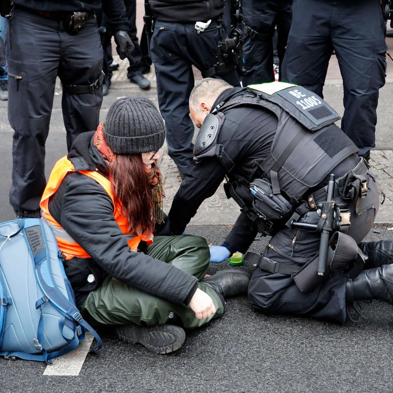 Eine Frau klebt sich auf der Straße fest und ein Polizist versucht sie zu entfernen