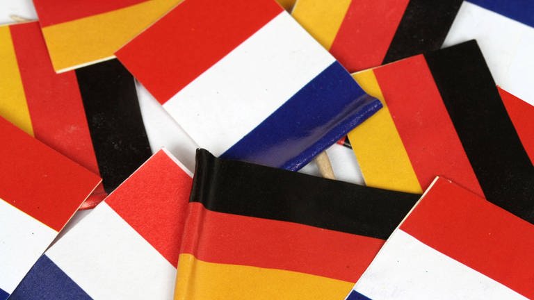 Flaggen der Republik Frankreich und Bundesrepublik Deutschland liegen auf einem Stapel (Foto: IMAGO, Ralph Peters)
