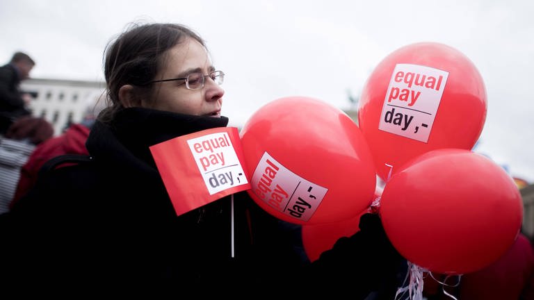 Demonstrantin mit Fahne und Ballon bei einer Kundgebung zum Equal Pay Day  (Foto: IMAGO, IMAGO / IPON)