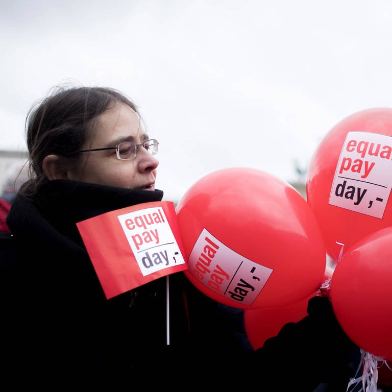 Demonstrantin mit Fahne und Ballon bei einer Kundgebung zum Equal Pay Day 