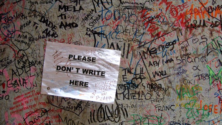 Namen und Schrift, Gekritzel an einer Wand. Darauf ist ein Papierschild geklebt mit der Aufschrift "Please don´t write here"  (Foto: IMAGO, PantherMedia / Marisa Cvitanovic)