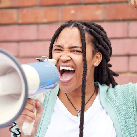 Eine schwarze Frau hebt ihren Arm und spricht durch ein Megafon
