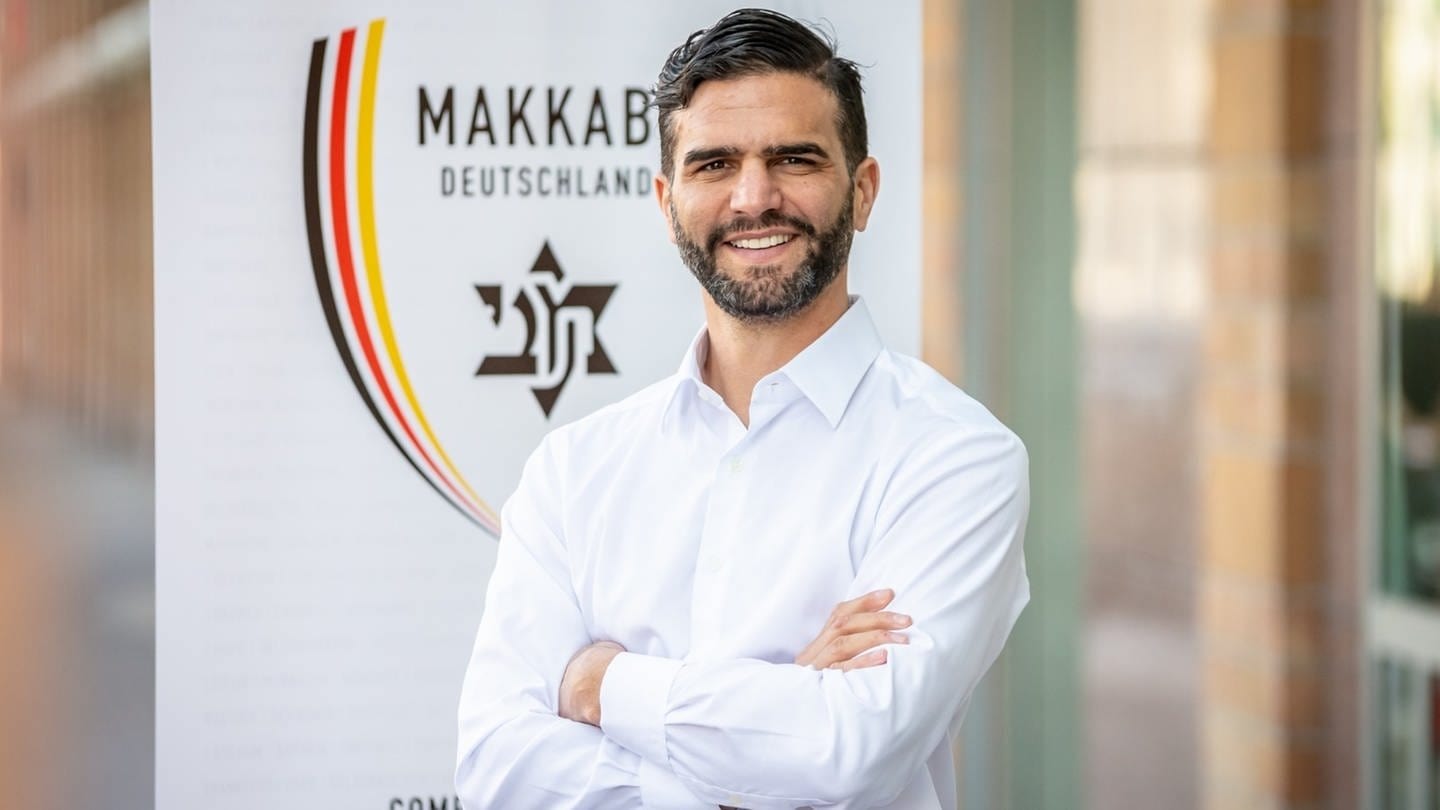 Alon Meyer, Präsident von Makkabi Deutschland, steht vor dem Logo. (Foto: dpa Bildfunk, picture alliance/dpa/MAKKABI Deutschland e. V. | .)