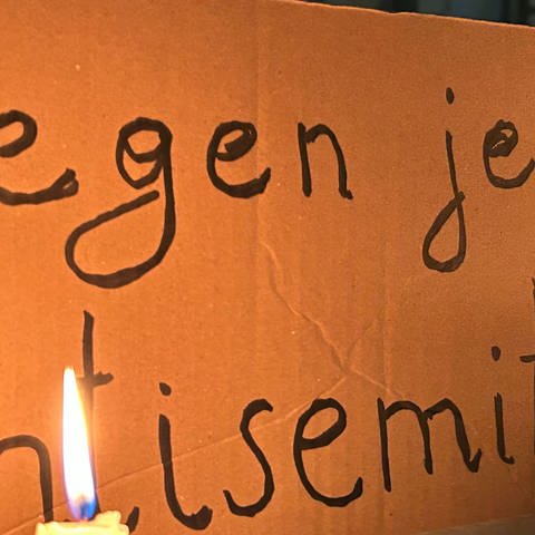Eine brennende Kerze steht vor einem Schild mit der Aufschrift "Gegen jeden Antisemitismus"