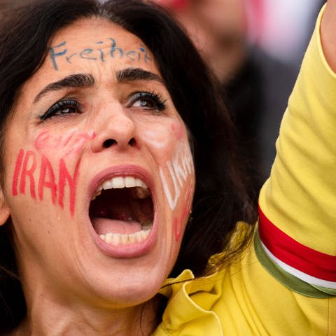 Junge Demonstrantin mit dem Schriftzug "Iran" im Gesicht.