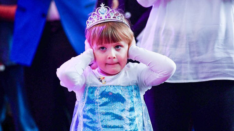 Ein kleines Mädchen, verkleidet als Prinzessin, hält sich die Ohren zu