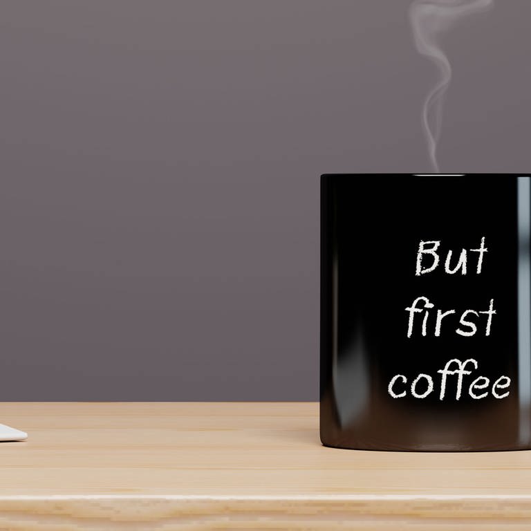Black mug with the inscription But first coffee on an office table. Symbolfoto