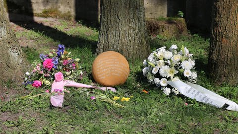 Gedenkkugel aus Ton, die zwischen zwei Blumensträußen liegt. (Foto: Gedenkstätte Ravensbrück)