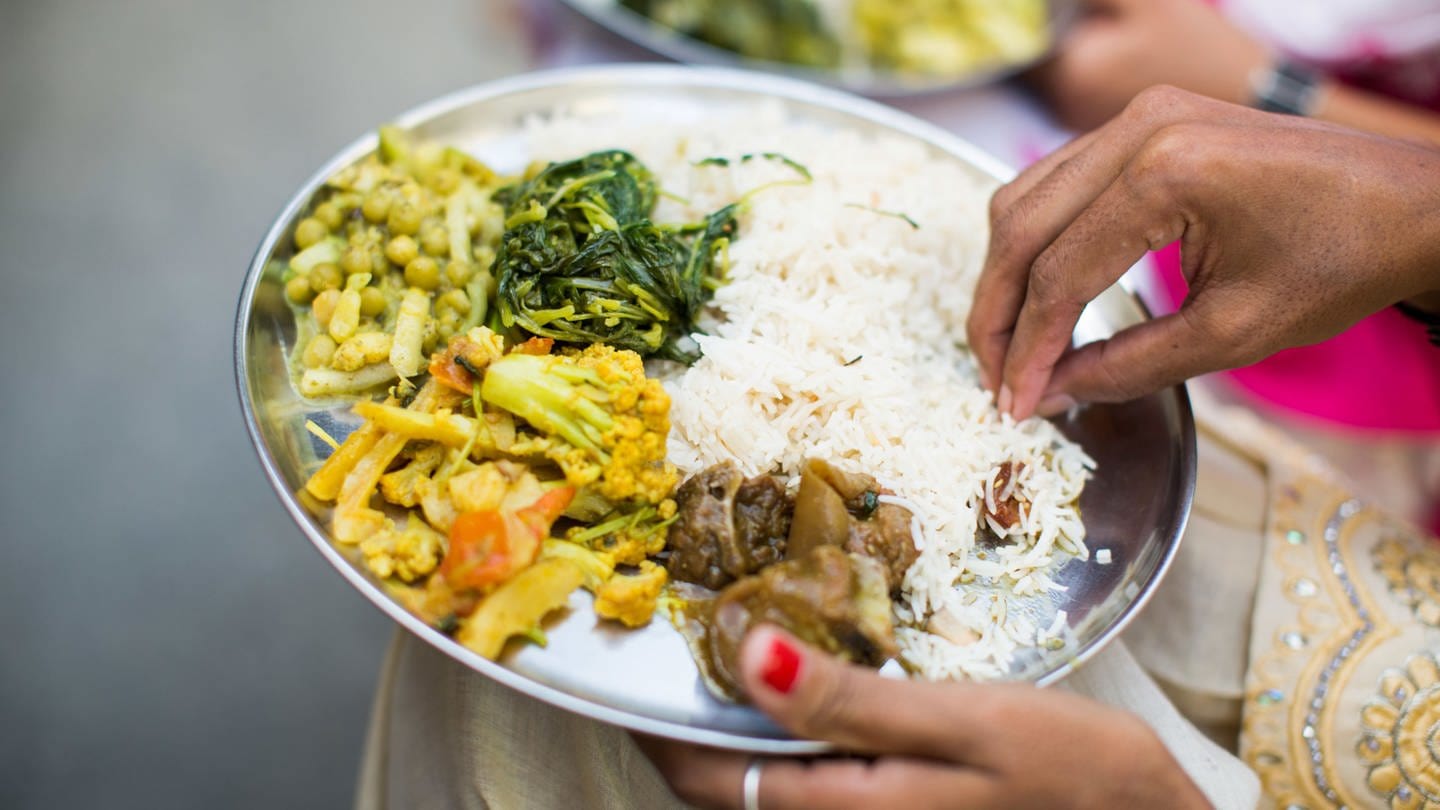 Indischer weiblich essender traditionelle dish mit rice, peas, Fleisch und Gemüse. Symbolfoto (Foto: IMAGO, Wirestock)