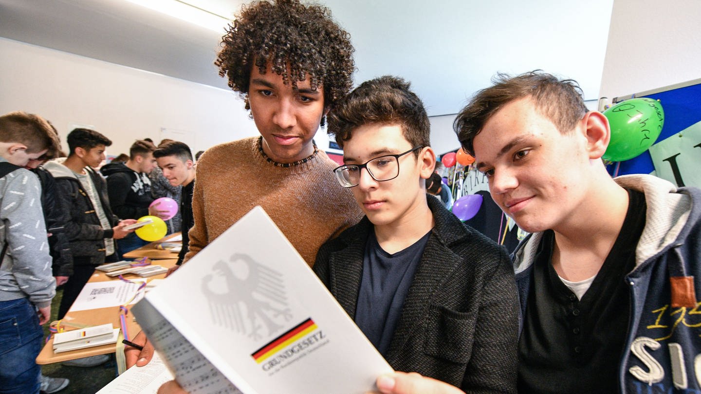 Drei männliche Schüler halten das Grundgesetz in den Händen (Foto: IMAGO, IMAGO / Funke Foto Services / Lutz von Staegmann)