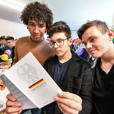 Drei männliche Schüler halten das Grundgesetz in den Händen