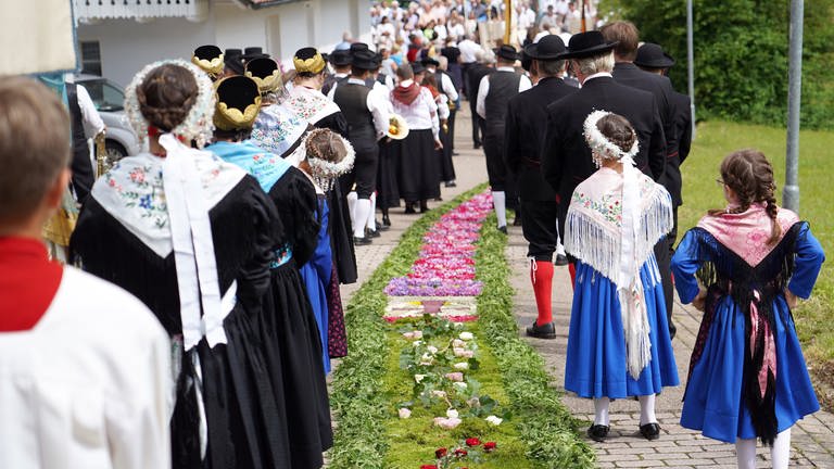 Gläubige gehen während der Fronleichnams-Prozession an einem Blumenteppich entlang. 