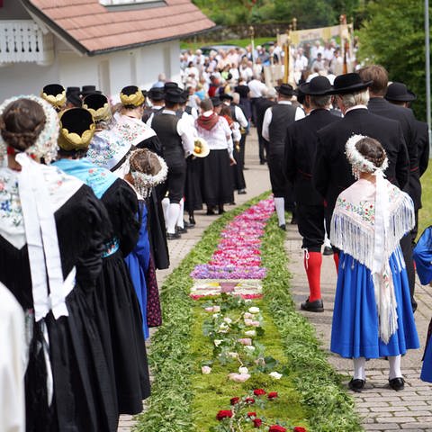 Gläubige gehen während der Fronleichnams-Prozession an einem Blumenteppich entlang. 