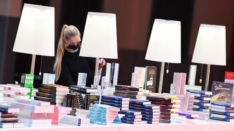 Eine Frau mit Alltagsmaske schaut auf einem Büchertisch in ein Buch