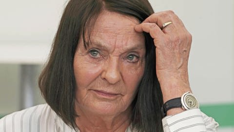 Die Autorin Monika Maron 2018 bei der Leipziger Buchmesse: Eine ältere Frau mit faltigem Gesicht und kinnlangen, braunen Haaren, die sie sich mit der Hand hinter ein Ohr streicht. Sie trägt eine gestreifte Bluse. (Foto: IMAGO, IMAGO / Gerhard Leber)