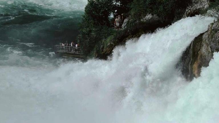 Der Rheinfall bei Schaffhausen. Wassergischt spritzt hoch. Besucher drängen sich am Rand. (Foto: SWR, Corso Verlag - Foto: Tom Krausz)