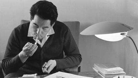 Der Autor Tschingis Aitmatow 1966 zündet sich an einem Schreibtisch eine Zigarette an  (Foto: IMAGO, IMAGO/ITAR-TASS/IMAGO/Viktor Koshevoi; )