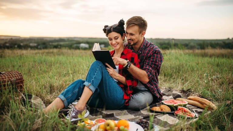Ein glückliches Paar sitzt auf einer Picknickdecke und schaut gemeinsam in ein Buch
