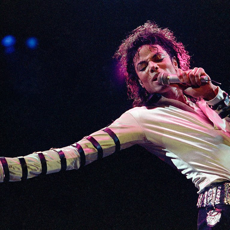 Michael Jackson in einem weiß-glänzenden Oberteil beim Singen auf einer Bühne