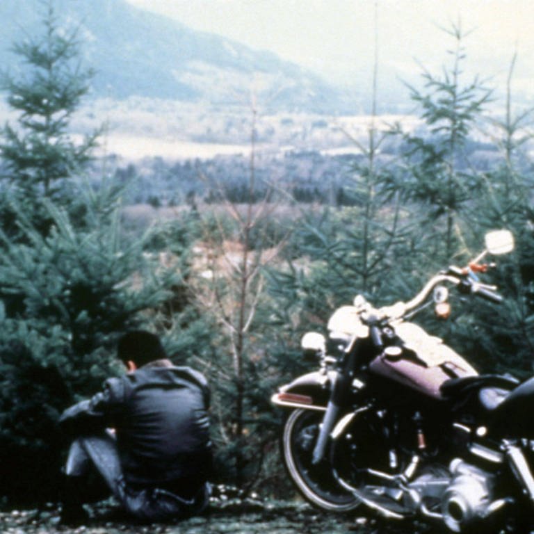 Ein Bild aus der ersten Staffel Twin Peaks zeigt einen jungen Mann, der neben seinem Motorrad sitzt und in ein Tal voller Nadelbäume blickt (Foto: IMAGO, xAaronxSpellingxProds/CourtesyxEverettxCollectionx)