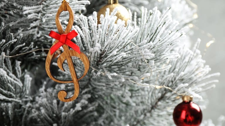 Ein Weihnachtsanhänger der eine Note darstellt hängt an einem weißen Baum 