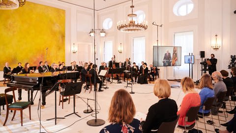 Die Berliner Philharmoniker sitzen im Schloss Bellevue vor ein paar Dutzend Zuschauern während Bundespräsident Frank-Walter Steinmeier wegen Krankheit per Video zugeschaltet ist. (Foto: picture-alliance / Reportdienste, Foto: Annette Riedl)