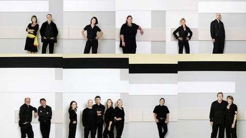 Mitglieder des SWR Vokalensembles Stuttgart  stehen einzeln oder in Grüppchen vor einer hellen Wand (Foto: SWR, SWR -)